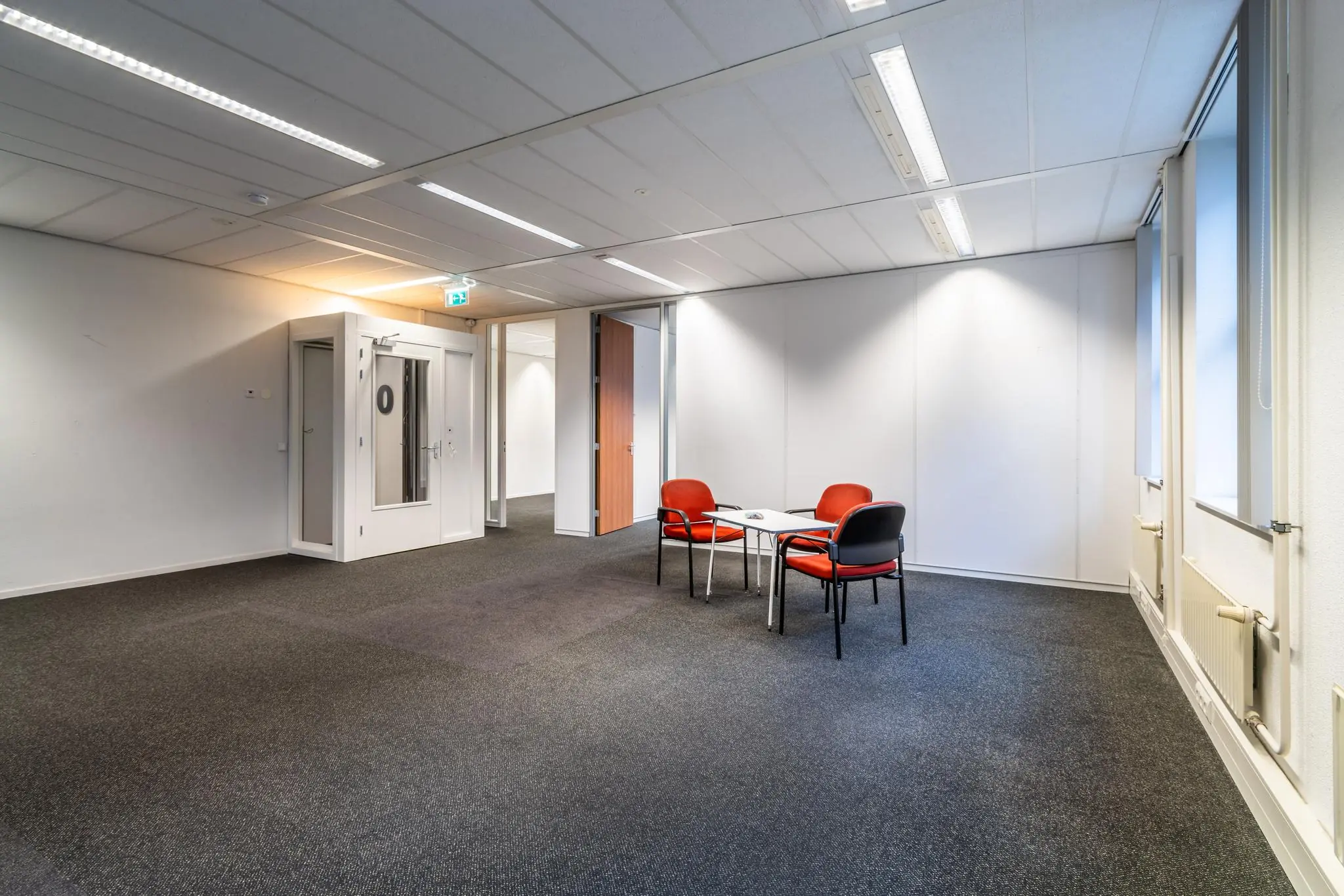 Kleine vergaderruimte in een kantoorpand aan de Lange Dreef met vier rode stoelen en een witte tafel.